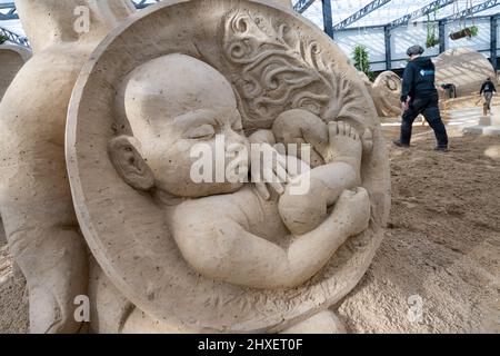 Binz, Deutschland. 11. März 2022. Die Sandskulptur eines Babys der Sandskulptur zeigt 'What a wonderful world'. Die Skulpturen zeigen Landschaften, Menschen und Fabelwesen. Quelle: Stefan Sauer/dpa/Alamy Live News Stockfoto