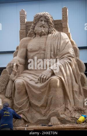 Binz, Deutschland. 11. März 2022. Ein Mann arbeitet an einer Sandskulptur von Zeus, dem Vater der Götter, der Sandskulptur Show "What a wonderful world". Die Skulpturen zeigen Landschaften, Menschen und Fabelwesen. Quelle: Stefan Sauer/dpa/Alamy Live News Stockfoto