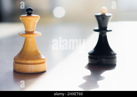 Schachfiguren, die in Sonnenlicht getaucht sind. Weiße und schwarze Königinnen. Weiß im Fokus, Schwarz verschwommen. Die Abstraktion der Konfrontation. Unternehmen. Stockfoto