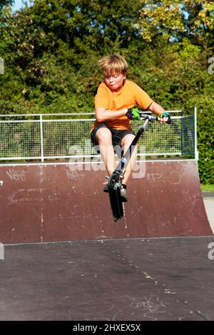 Junge springt mit einem Motorroller über einen Dorn in den Skate Park und genießen es Stockfoto