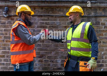 Freundliche, fröhliche und lächelnde Bauarbeiter grüßen und schütteln sich die Hände. Stockfoto