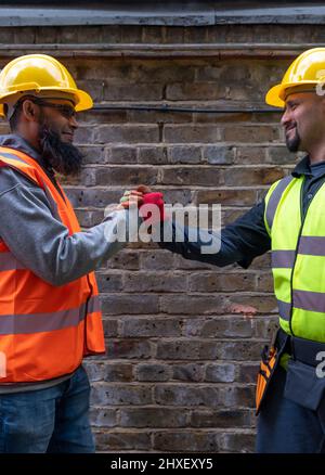 Freundliche, fröhliche und lächelnde Bauarbeiter grüßen und schütteln sich die Hände. Stockfoto