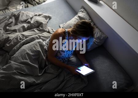 Hübsche Frau mittleren Alters mit Ihrem Tablet-PC vor dem Schlafen im Bett am Abend Stockfoto