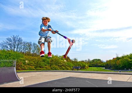 Junge springt mit einem Motorroller über einen Dorn in den Skate Park und genießen es Stockfoto