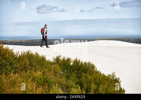 Wandern durch die Wildnis. Aufnahme eines jungen Wanderers, der entlang der Sanddünen läuft. Stockfoto