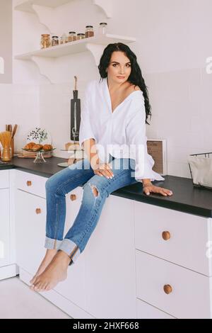 Brunette schöne stilvolle Frau in weißem Hemd und Jeans in der Küche. Koch- und Modekonzept Stockfoto
