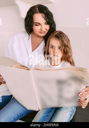 Schöne stilvolle Brünette Frau mit entzückenden Tochter lesen aktuelle Nachrichten in Papierzeitung. Familie, Zeitung, Nachrichten, Schock, Liebe, Support-concep Stockfoto