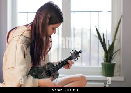 Neue Hobbys von Teenagern, ein Mädchen lernt, eine Ukulele-Gitarre zu Hause zu spielen Stockfoto