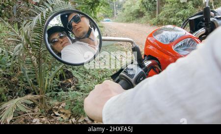 Liebe Paar auf roten Motorrad in weißen Kleidern auf Wald Road Trail Reise zu gehen. Blick in den Rückspiegel. Zwei kaukasische Touristen Mann fahren weiter Stockfoto