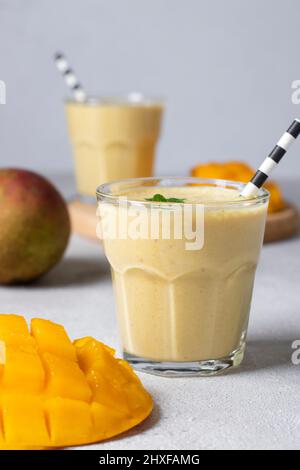 Mango Lassi in zwei Gläsern auf hellgrauem Hintergrund. Frische indischer Lassi aus Joghurt, Wasser, Gewürzen, Mango und Eis Stockfoto