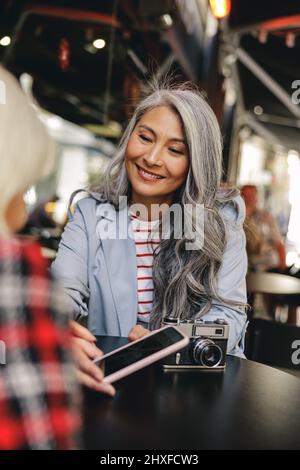Attraktive reife Frau mit Smartphone im Café Stockfoto