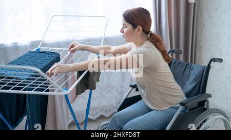 Kaukasische Frau im Rollstuhl hängt nasse Wäsche an einem Trockner. Stockfoto