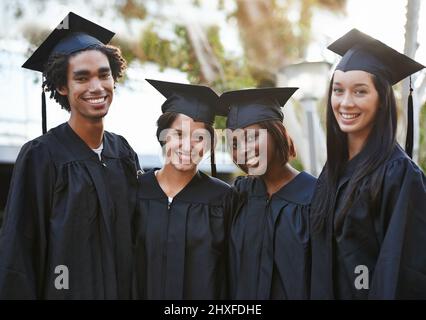 Sie haben eine strahlende Zukunft vor sich. Eine Gruppe lächelnder Hochschulabsolventen, die in Mütze und Kleid zusammenstehen. Stockfoto