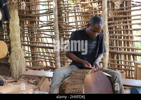 Mpigi, Uganda. 10. März 2022. Ein Trommelmacher arbeitet an einer Trommel im Dorf Mpambire im Bezirk Mpigi, Uganda, 10. März 2022. Mpambire, ein Dorf im zentralen ugandischen Bezirk Mpigi, ist als Geburtsort der Trommeln im Land bekannt. Das Dorf ist übersät mit provisorischen Werkstätten, in denen die Trommeln aus Baumstämmen und Tierfellen hergestellt werden.ZUM THEMA "Feature: Jahrhundertealte Tradition der Trommelherstellung in Uganda im Kampf gegen die Moderne" Quelle: Zhang Gaiping/Xinhua/Alamy Live News Stockfoto