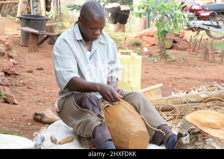 Mpigi, Uganda. 10. März 2022. Francis Yiga, ein Handwerker, arbeitet auf einer Trommel im Dorf Mpambire im Bezirk Mpigi, Uganda, 10. März 2022. Mpambire, ein Dorf im zentralen ugandischen Bezirk Mpigi, ist als Geburtsort der Trommeln im Land bekannt. Das Dorf ist übersät mit provisorischen Werkstätten, in denen die Trommeln aus Baumstämmen und Tierfellen hergestellt werden.ZUM THEMA "Feature: Jahrhundertealte Tradition der Trommelherstellung in Uganda im Kampf gegen die Moderne" Quelle: Zhang Gaiping/Xinhua/Alamy Live News Stockfoto