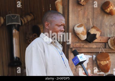 Mpigi, Uganda. 10. März 2022. Francis Yiga, ein Handwerker, spricht in einem Interview mit Xinhua im Dorf Mpambire im Bezirk Mpigi, Uganda, 10. März 2022. Mpambire, ein Dorf im zentralen ugandischen Bezirk Mpigi, ist als Geburtsort der Trommeln im Land bekannt. Das Dorf ist übersät mit provisorischen Werkstätten, in denen die Trommeln aus Baumstämmen und Tierfellen hergestellt werden.ZUM THEMA "Feature: Jahrhundertealte Tradition der Trommelherstellung in Uganda im Kampf gegen die Moderne" Quelle: Zhang Gaiping/Xinhua/Alamy Live News Stockfoto