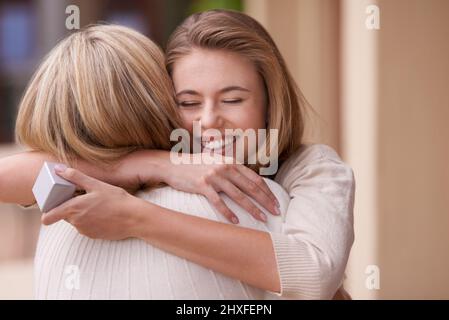 Ich liebe dich, Mama. Eine Tochter umarmte ihre Mutter, nachdem sie ein Geschenk erhalten hatte. Stockfoto