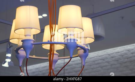 Nahaufnahme eines Kronleuchters, der auf weißem Deckenhintergrund hängt. HDR. Ungewöhnliche Hängelampe mit orangefarbenen Drähten, violettem Metallrand und beigefarbenen Leuchten. Stockfoto