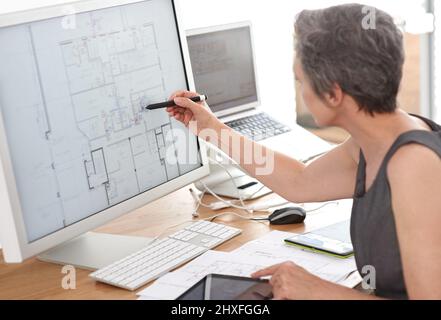 Zukunftsorientierte Architektur. Eine reife Architektin, die an Bauplänen auf ihrem Touchscreen-Computer arbeitet. Stockfoto