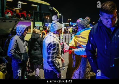 Ein Flüchtling mit ukrainischer Flagge, vor einem Bus gesehen. Ein ehemaliges Einkaufszentrum in Przemysl - von Freiwilligen in eines der größten Flüchtlingshilfezentren der Region verwandelt. Seit Beginn der russischen Invasion in der Ukraine sind über 1,4 Millionen Menschen nach Polen geflohen, um dem Krieg zu entkommen. Ukrainische Flüchtlinge werden mit komplexer Unterstützung sowohl von Wohltätigkeitsorganisationen als auch von einfachen Polen begrüßt, aber viele humanitäre Experten weisen darauf hin, dass bei einem so großen Zustrom von Menschen und nicht ausreichender Unterstützung durch die polnische Regierung innerhalb weniger Wochen eine Krise eintreten könnte. Stockfoto