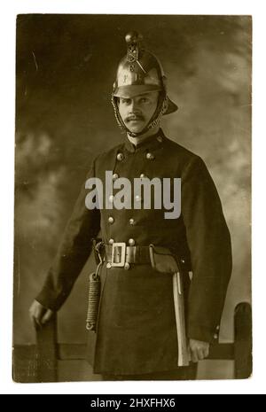 Originalpostkarte aus dem frühen 20. Jahrhundert mit einem schönen Feuerwehrmann in der Feuerwehruniform von Eastbourne - mit einer Axt und einem Seil am Gürtel befestigt, mit einem Messinghelm, Studio of the Eastbourne Stereoscopic Co., Großbritannien um 1915 Stockfoto