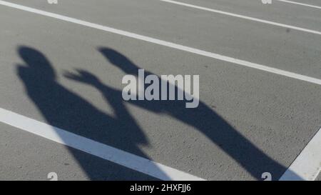 Die Silhouetten zweier junger Männer während wütender Konflikte. HDR. Schatten von miteinander streitenden Freunden auf dem Hintergrund des Parkasphalts. Stockfoto