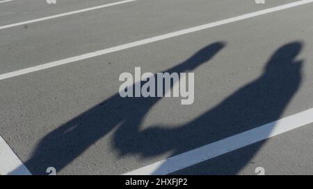 Die Silhouetten zweier junger Männer während wütender Konflikte. HDR. Schatten von miteinander streitenden Freunden auf dem Hintergrund des Parkasphalts. Stockfoto