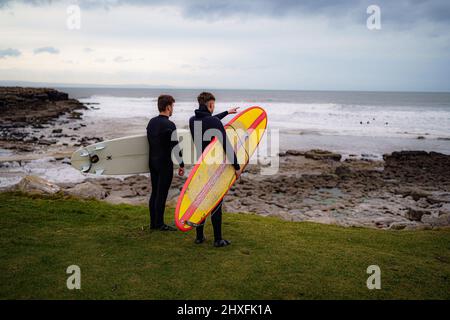 Surfer beobachten die Wellen in Rest Bay in Porthcawl, während über das Wochenende eine gelbe Windwarnung in West Wales in Kraft ist. Bilddatum: Samstag, 12. März 2022. Stockfoto