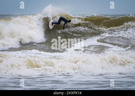 Surfer reiten in Rest Bay in Porthcawl auf den Wellen, während über das Wochenende eine gelbe Windwarnung in West Wales in Kraft ist. Bilddatum: Samstag, 12. März 2022. Stockfoto