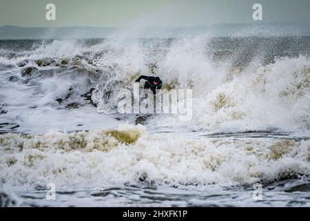 Surfer reiten in Rest Bay in Porthcawl auf den Wellen, während über das Wochenende eine gelbe Windwarnung in West Wales in Kraft ist. Bilddatum: Samstag, 12. März 2022. Stockfoto