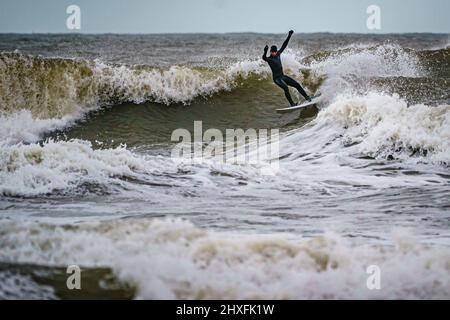 Surfer reiten in Rest Bay in Porthcawl auf den Wellen, während über das Wochenende eine gelbe Windwarnung in West Wales in Kraft ist. Bilddatum: Samstag, 12. März 2022. Stockfoto