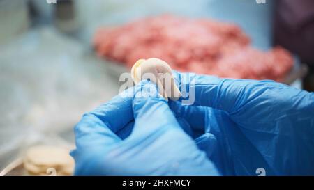 Produktion im Lebensmittelgeschäft. Clip. Eine Frau in einer speziellen Schürze und Handschuhen macht Knödel auf einem speziellen Eisentisch. Stockfoto