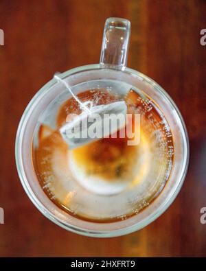 Teebeutel in Wasser brauen - Koffein-Getränk in doppelverglasten Teetassen - Nahaufnahme eines teilweise gebrühten Teebeutels in einer Teetasse mit heißem Wasser Stockfoto