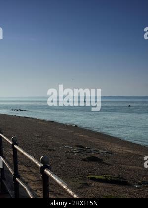 Gebleichte, dramatische Aussicht über den Solent von der Isle of Wight, über Kiesstrand und das wellige Meer zu den silhouettierten Hügeln des Festlandes. Stockfoto