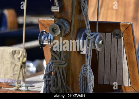 Antike hölzerne Segelbootrollen und Seile, die auf dem Boden eines Holzmastes gebunden sind. Stockfoto