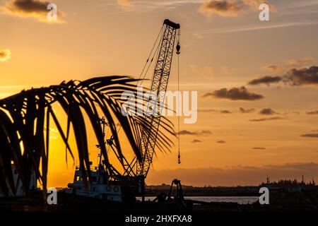 Kran, Baumaschinen, auf einem Boot. Foto aufgenommen bei Sonnenuntergang in Kuba. Kontrastreiche Fotografie in Orange und Schwarz. Stockfoto