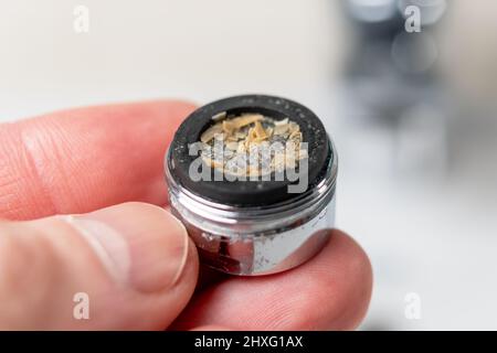 Ein verstopfter verschmutzter Wasserhahn-Belüfter mit Calciumplaque in der Hand eines Klempners. Hahn-Filter über dem Waschbecken. Makroaufnahme. Hauswartungskonzept. Stockfoto