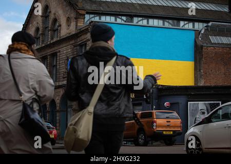 Glasgow, Großbritannien, 12.. März 2022. Die ukrainische Flagge wurde an einer Wand über der Clutha & Victoria Bar angebracht, was die Unterstützung der Ukraine in ihrem aktuellen Krieg mit Präsident PutinÕs Russland in Glasgow, Schottland, am 12. März 2022, zeigt. Foto: Jeremy Sutton-Hibbert/ Alamy Live News. Stockfoto