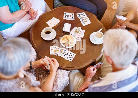 Gewinnen durch eine Kombination aus Glück und Geschick. Eine Gruppe von Senioren, die in ihrem Altersheim Karten um einen Tisch spielen, in einem Hochwinkel fotografiert. Stockfoto