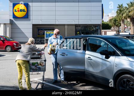 Kunden legen ihre Lebensmittel in ihr Auto, als sie den deutschen internationalen Discounter-Supermarkt Lidl, gesehen in Spanien, verlassen. Stockfoto