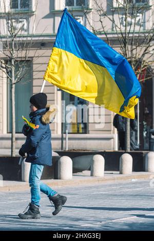 Kind oder Kind mit Winterkleidung, ukrainischer Flagge und Hut. Protest gegen den Krieg in der Ukraine, verursacht von Putin und Russland, vertikal Stockfoto