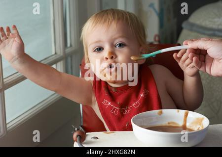 Wachsender Junge braucht sein Essen. Ein kleiner Junge, der in seinem Hochstuhl nach Herzenslust isst. Stockfoto