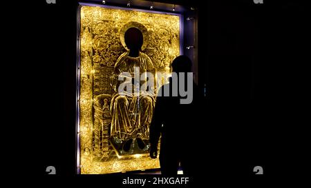 Rückansicht eines Mannes, der unter dem Schutzglas der heiligen goldenen Ikone nahe kommt. Konzept. Das Innere der orthodoxen Kirche dunkler Saal. Stockfoto