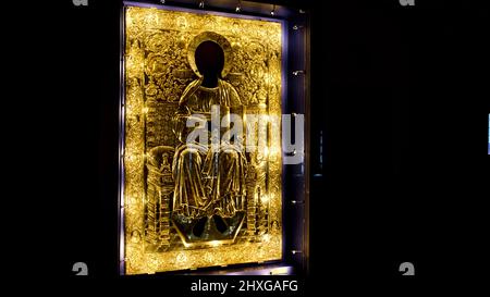 Rückansicht eines Mannes, der unter dem Schutzglas der heiligen goldenen Ikone nahe kommt. Konzept. Das Innere der orthodoxen Kirche dunkler Saal. Stockfoto