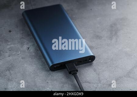 Tragbare externe Akku-Powerbank blau mit USB-Kabel auf einem dunklen strukturierten Hintergrund zum Laden von Gadgets Stockfoto