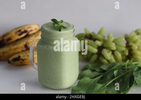 Grüner Smoothie aus gefrorenen grünen Trauben, frischem Babyspinat, Bananen und Mandelmilch. Serviert im Einmachglas. Aufgenommen auf weißem Hintergrund. Stockfoto