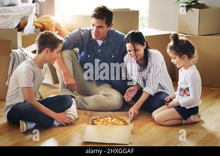 Essen eins und viele weitere werden kommen. Aufnahme einer glücklichen jungen Familie, die gemeinsam Pizza in ihrem neuen Zuhause hat. Stockfoto