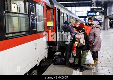 München, Deutschland. 12. März 2022. Eine Gruppe von Flüchtlingen aus der Ukraine steht mit Helfern des Roten Kreuzes auf dem Bahnsteig des Münchner Hauptbahnhofs, nachdem sie mit einem Sonderzug mit rund 400 Flüchtlingen aus der Ukraine angekommen sind. Der Zug mit ursprünglich rund 1500 Flüchtlingen kommt aus dem polnischen Dorf Dorohusk an der Grenze zur Ukraine - viele Flüchtlinge waren bereits an anderen Bahnhöfen abgestiegen. Quelle: Matthias Balk/dpa/Alamy Live News Stockfoto