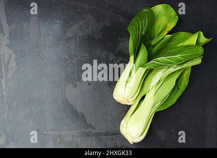 Grün und grün. Draufsicht auf Blätter von chinakohl, die auf einer dunklen Arbeitsplatte liegen. Stockfoto