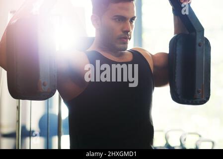 Das Fitnessstudio ist gebunden, es gibt kein Aufgeben. Eine kurze Aufnahme eines hübschen jungen Sportlers, der in einem Fitnessstudio mit einem Trainingsgerät trainiert. Stockfoto